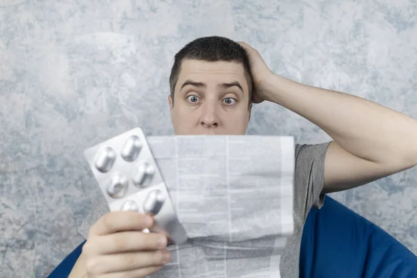 Man on a white background reads the instructions for medicines. Male looks at the list and composition of the drug. The concept of home self-medication and the study of the properties of drugs