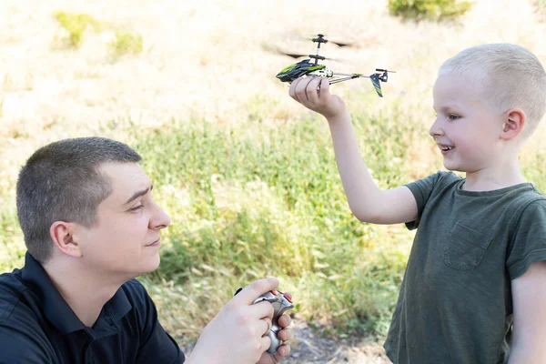Dad and child playing with radio-controlled helicopter. Blond boy holds in his hand a mini-model of a helicopter in which propellers work. Kid develops fine motor skills. Happy childhood and love