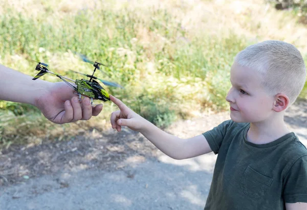 Dad and child playing with radio-controlled helicopter. Blond boy holds in his hand a mini-model of a helicopter in which propellers work. Kid develops fine motor skills. Happy childhood and love