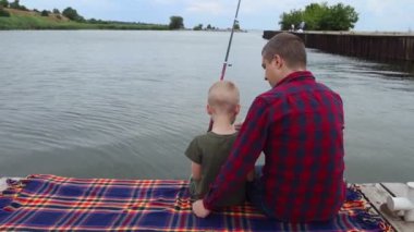 Baba oğul balık tutuyor. Baba oğluna makarayı nasıl tutup döndüreceğini gösteriyor. Gölde ya da nehirde balık tutma eğitimi. İlgili ebeveyn kavramı.