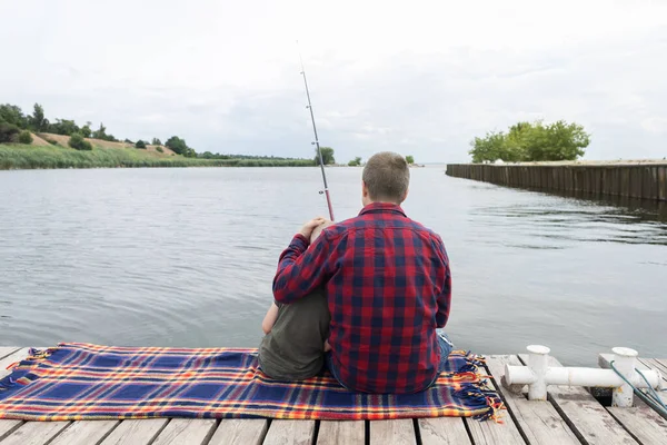 Father and son fishing. Dad shows his son how to hold the spinning and spin the reel. Fishing training on a pond or river. Caring parent concept.