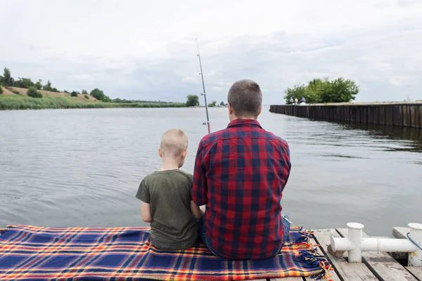 Father and son fishing. Dad shows his son how to hold the spinning and spin the reel. Fishing training on a pond or river. Caring parent concept.