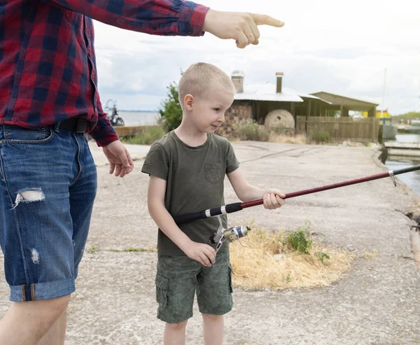 Father and son fishing. Dad shows his son how to hold the spinning and spin the reel. Fishing training on a pond or river. Caring parent concept.