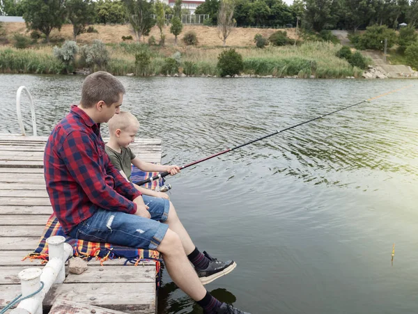 Father and son fishing. Dad shows his son how to hold the spinning and spin the reel. Fishing training on a pond or river. Caring parent concept.