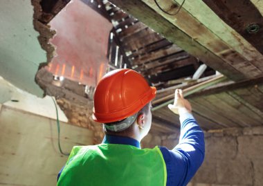 Building inspector. Man in a hard hat and a yellow reflective vest examines damaged structures and inspects the building. Damage assessment. Preparing for the repair or construction of a building