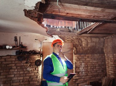 Building inspector. Man in a hard hat and a yellow reflective vest examines damaged structures and inspects the building. Damage assessment. Preparing for the repair or construction of a building