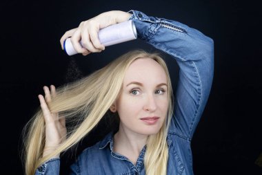 Dry shampoo. Blonde girl sprays shampoo on her hair. The problem of oily hair while traveling. An emergency remedy for excessive sebum production. Make your head clean without water