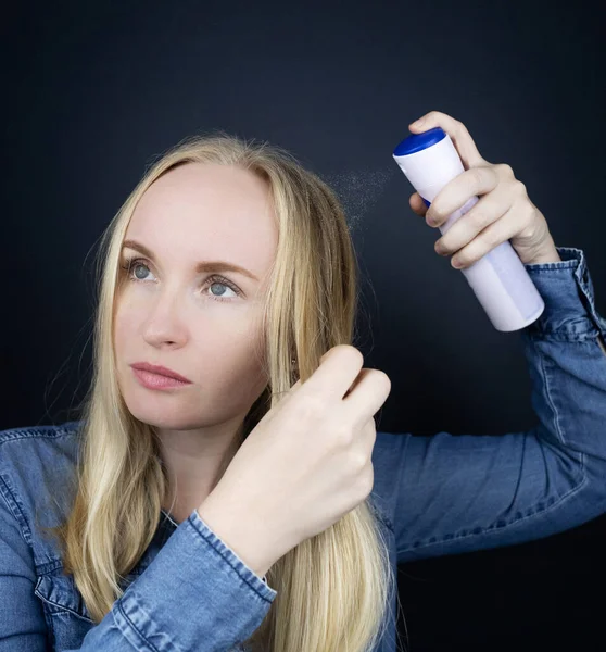 Dry shampoo. Blonde girl sprays shampoo on her hair. The problem of oily hair while traveling. An emergency remedy for excessive sebum production. Make your head clean without water