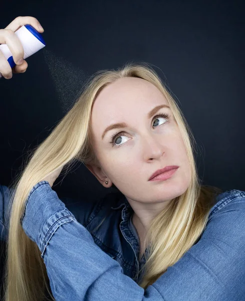 Dry shampoo. Blonde girl sprays shampoo on her hair. The problem of oily hair while traveling. An emergency remedy for excessive sebum production. Make your head clean without water