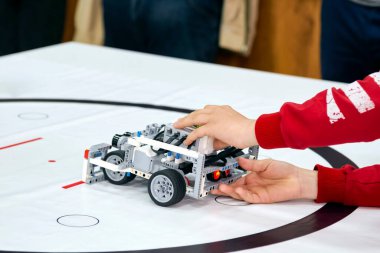 Robotics competitions. Kid's hands and a robot on wheels