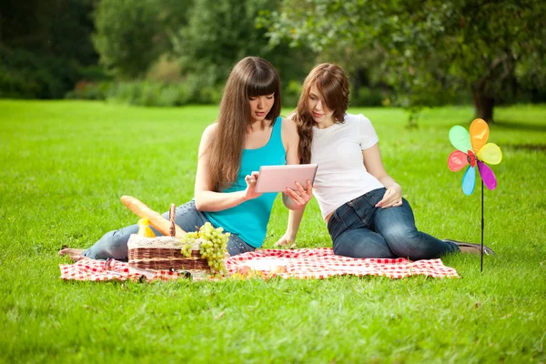 Två kvinnor i parken på en picknick och tablet pc — Stockfoto