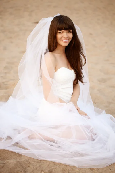 Beautiful bride with a long veil on the beach at sunset — Stock Photo, Image