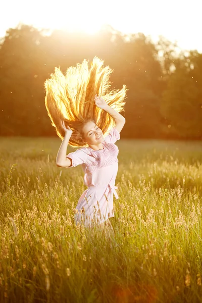 Mulher sorridente em um campo ao pôr-do-sol com cabelo voador — Fotografia de Stock