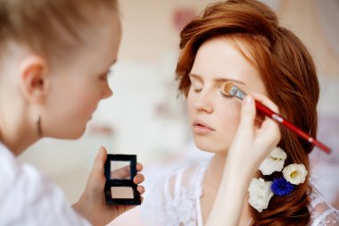 stylist maakt make-up bruid op de huwelijksdag