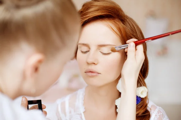 stylist maakt make-up bruid op de huwelijksdag