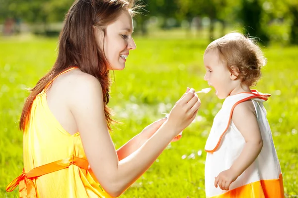 Mother feeds baby outdoors in the grass — Stock Photo, Image