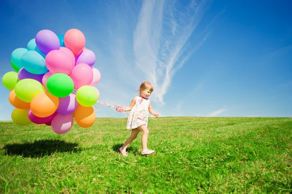 Weinig meisje bedrijf kleurrijke ballonnen. kind spelen op een groen — Stockfoto