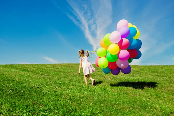 Liten flicka anläggning färgglada ballonger. barn som leker på en grön — Stockfoto