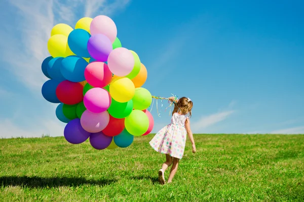 Μικρό κορίτσι εκμετάλλευση πολύχρωμα μπαλόνια. παιδί που παίζει σε μια Πράσινη — Φωτογραφία Αρχείου