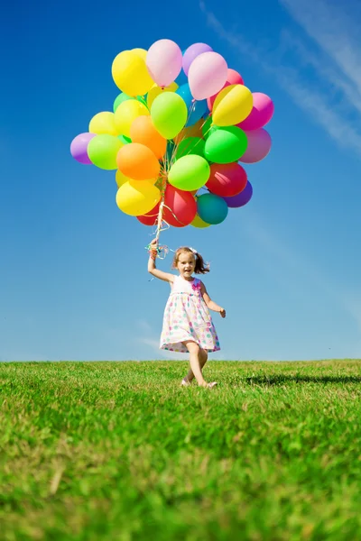 Küçük kız holding renkli balonlar. yeşil üzerinde oynayan çocuk — Stok fotoğraf