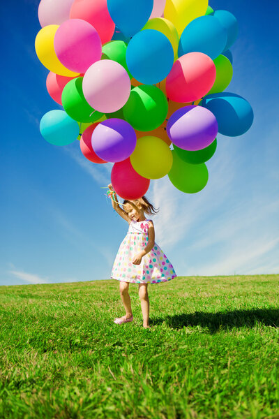 Little girl holding colorful balloons. Child playing on a green