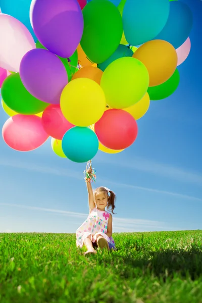 Маленькая девочка держит разноцветные шарики. Ребенок играет на зеленом — стоковое фото