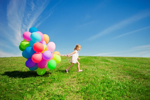 Weinig meisje bedrijf kleurrijke ballonnen. kind spelen op een groen — Stockfoto