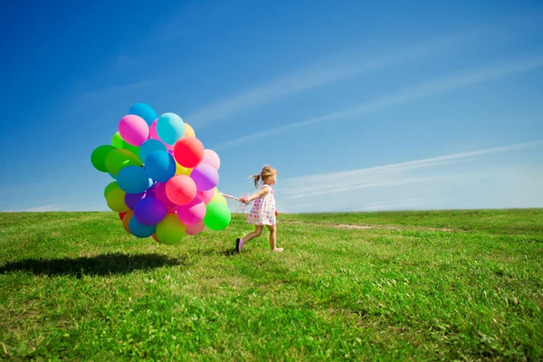 Weinig meisje bedrijf kleurrijke ballonnen. kind spelen op een groen — Stockfoto