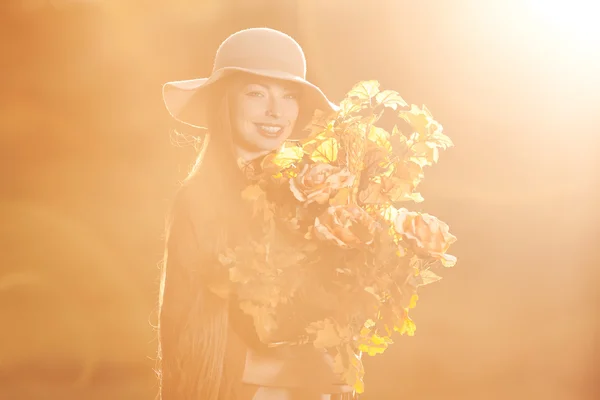 Jeune femme marchant dans le parc d'automne avec un bouquet de feuilles d'automne — Photo