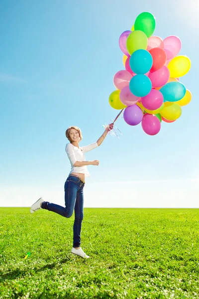 Jonge vrouw met ballonnen in handen in het gebied tegen de hemel — Stockfoto