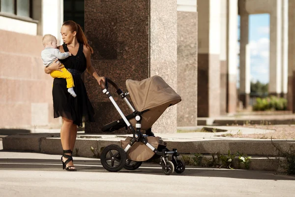 Mãe moderna na moda em uma rua de cidade com um carrinho de bebê. Jovem mo — Fotografia de Stock