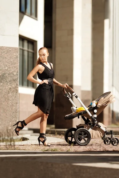 Trendiga moderna mor på en stadsgata med barnvagn. ung mamma — Stockfoto