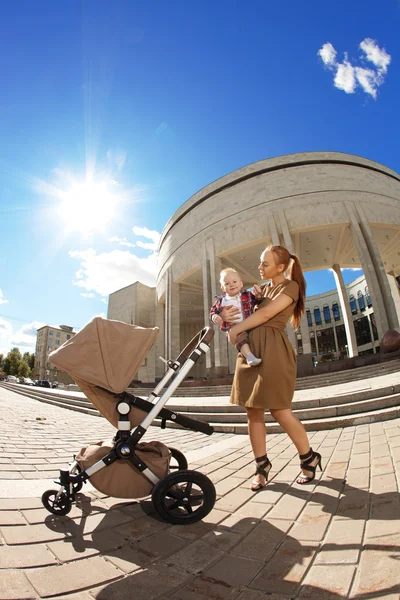 Modieuze moderne moeder op een stedelijke straat met een kinderwagen. jonge m — Stockfoto