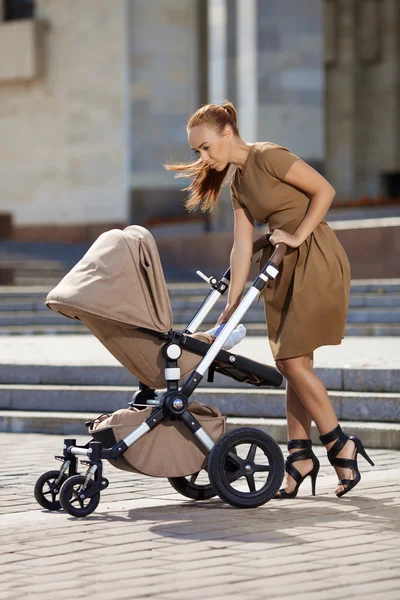 Fashionable modern mother on a urban street with a pram. Young m — Stock Photo, Image