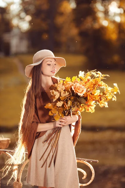 Giovane donna che cammina nel parco autunnale con un mazzo di lievito autunnale Immagine Stock