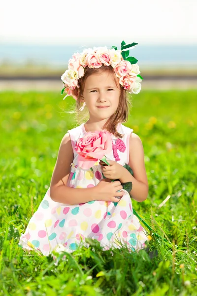 Schöne kleine Mädchen mit einer Rose in der Hand und einem Kranz von ro lizenzfreie Stockbilder