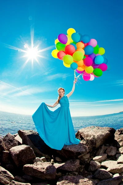 Luxusmode Frau mit Luftballons in der Hand am Strand gegen lizenzfreie Stockfotos