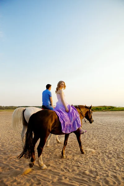 Dois cavaleiros a cavalo ao pôr-do-sol na praia. Os amantes montam cavalos — Fotografia de Stock