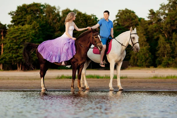 Dos jinetes a caballo al atardecer en la playa. Los amantes montan hors — Foto de Stock