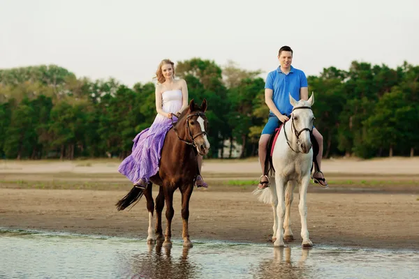 Due cavalieri a cavallo al tramonto sulla spiaggia. Gli amanti cavalcano antipasti — Foto Stock