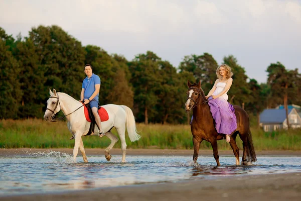 Due cavalieri a cavallo al tramonto sulla spiaggia. Gli amanti cavalcano antipasti — Foto Stock