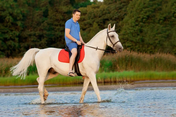 Giovanotto che cavalca un cavallo al tramonto sulla spiaggia. Uomo con un hors — Foto Stock