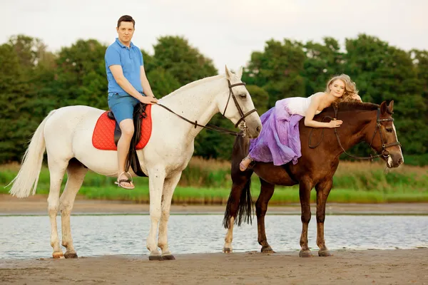 Due cavalieri a cavallo al tramonto sulla spiaggia. Gli amanti cavalcano antipasti — Foto Stock