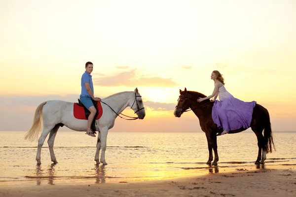 Dois cavaleiros a cavalo ao pôr-do-sol na praia. Os amantes montam cavalos — Fotografia de Stock