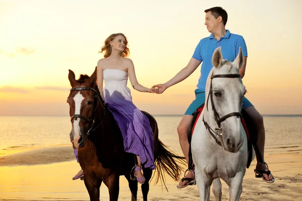 Dois cavaleiros a cavalo ao pôr-do-sol na praia. Os amantes montam cavalos — Fotografia de Stock