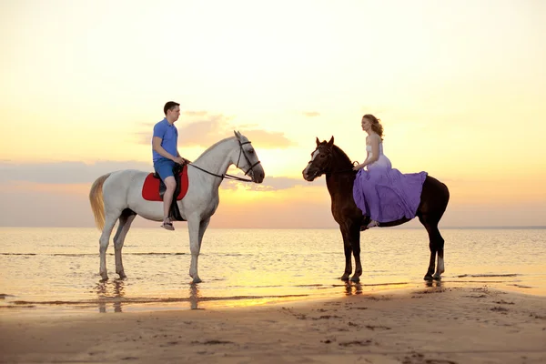 Twee renners te paard bij zonsondergang op het strand. liefhebbers rijden hors — Stockfoto