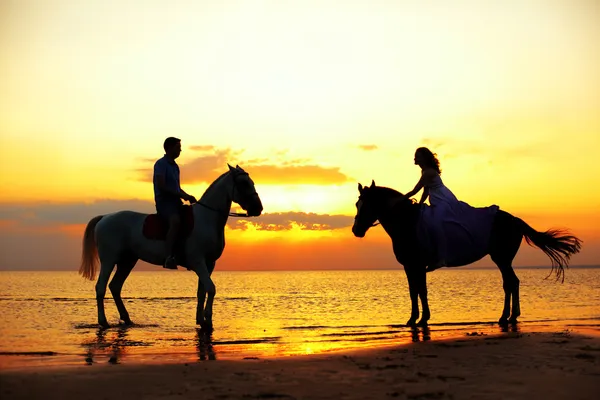 Dos jinetes a caballo al atardecer en la playa. Los amantes montan hors —  Fotos de Stock