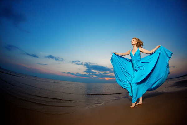 Luxury woman in a long blue evening  dress on the beach. Beauty 