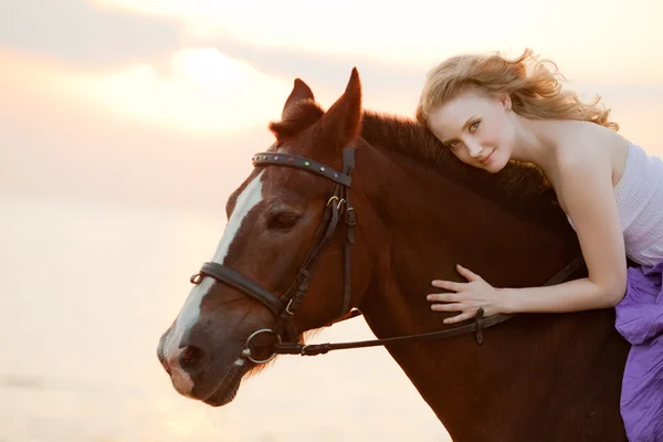 Hermosa mujer montando un caballo al atardecer en la playa. Joven gir Imagen de stock