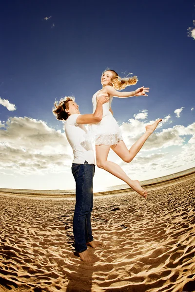 Glücklicher Mann, der eine Frau am Strand hält. verliebte Paare durch einen — Stockfoto